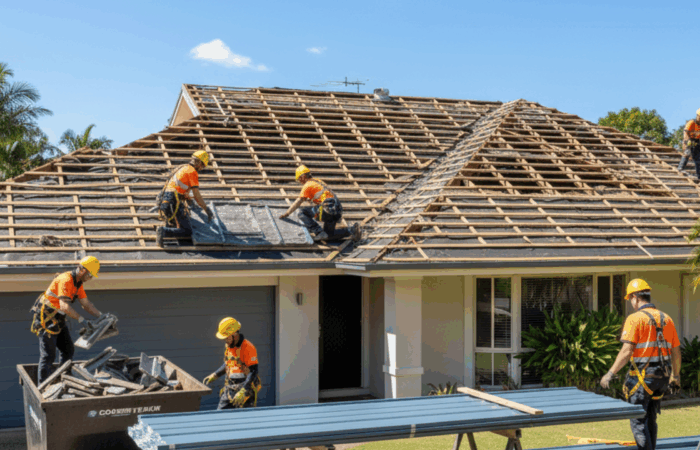 Roofers removing old roofing materials from a home and preparing for a new Colorbond installation under clear skies.
