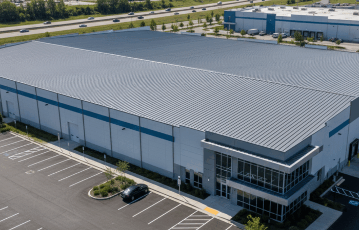 An aerial view of a large industrial warehouse with a new metal roof, clean lines, and a well-maintained exterior under clear skies.